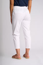 White cropped pants with an elastic waistband, shown from the back on a model wearing brown slide sandals against a light gray studio background.