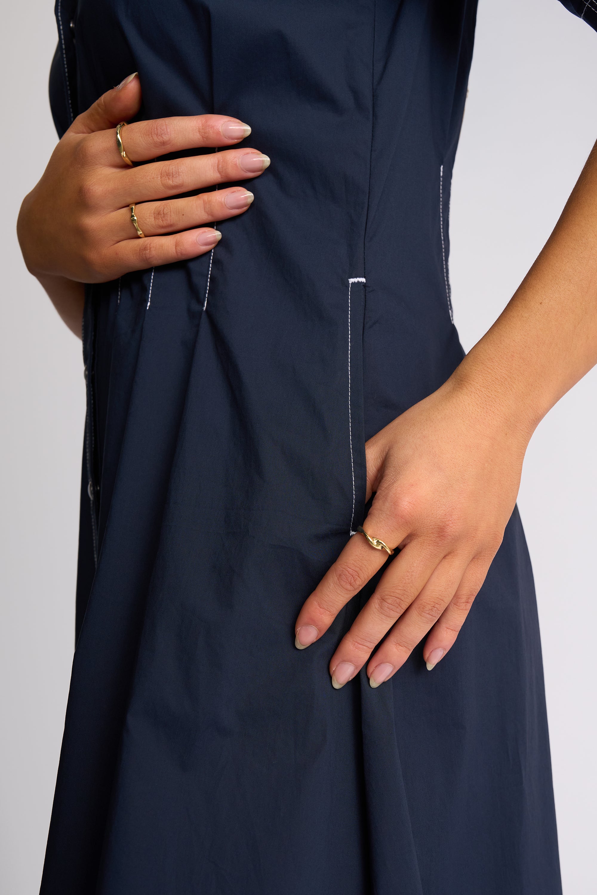 Close-up of a person wearing a dark navy dress, showing the side pocket with white contrast stitching and hands resting on the fabric against a light gray background.