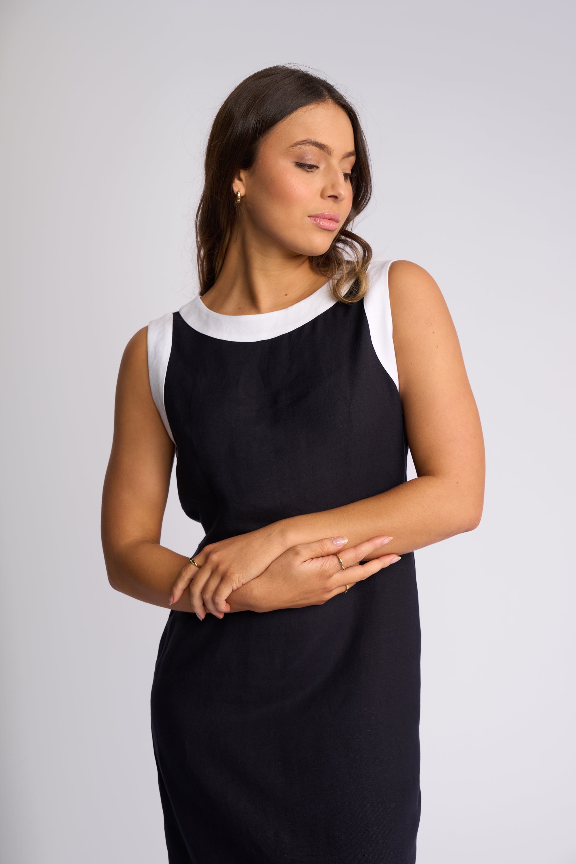 A woman modeling a sleeveless black dress with contrasting white trim at the crew neckline and under the arms, set against a plain light gray studio background.