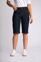 A person wearing dark navy denim biker shorts with rolled cuffs, paired with a white t-shirt and off-white sneakers, shown from the waist down against a light gray studio background.