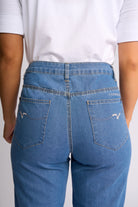Rear view of a person wearing light blue denim jeans with a white t-shirt, showing the back pockets and stitching details.