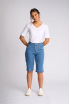 A woman modeling a white short-sleeve V-neck t-shirt and light blue denim capri jeans with white sneakers, standing against a light gray studio background.