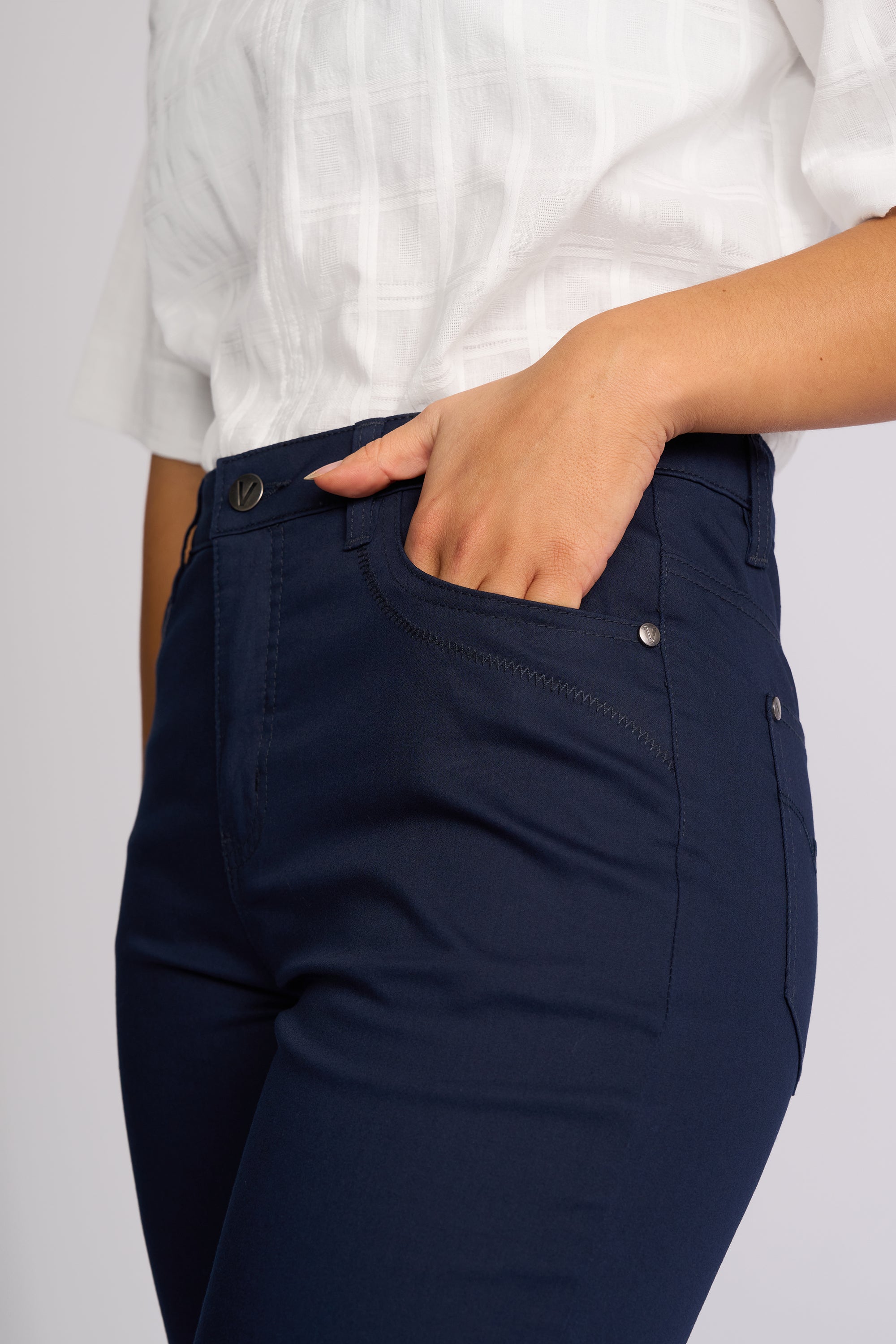 Close-up of a person wearing dark navy blue pants with a white top, showing the side pocket and hand in the pocket.