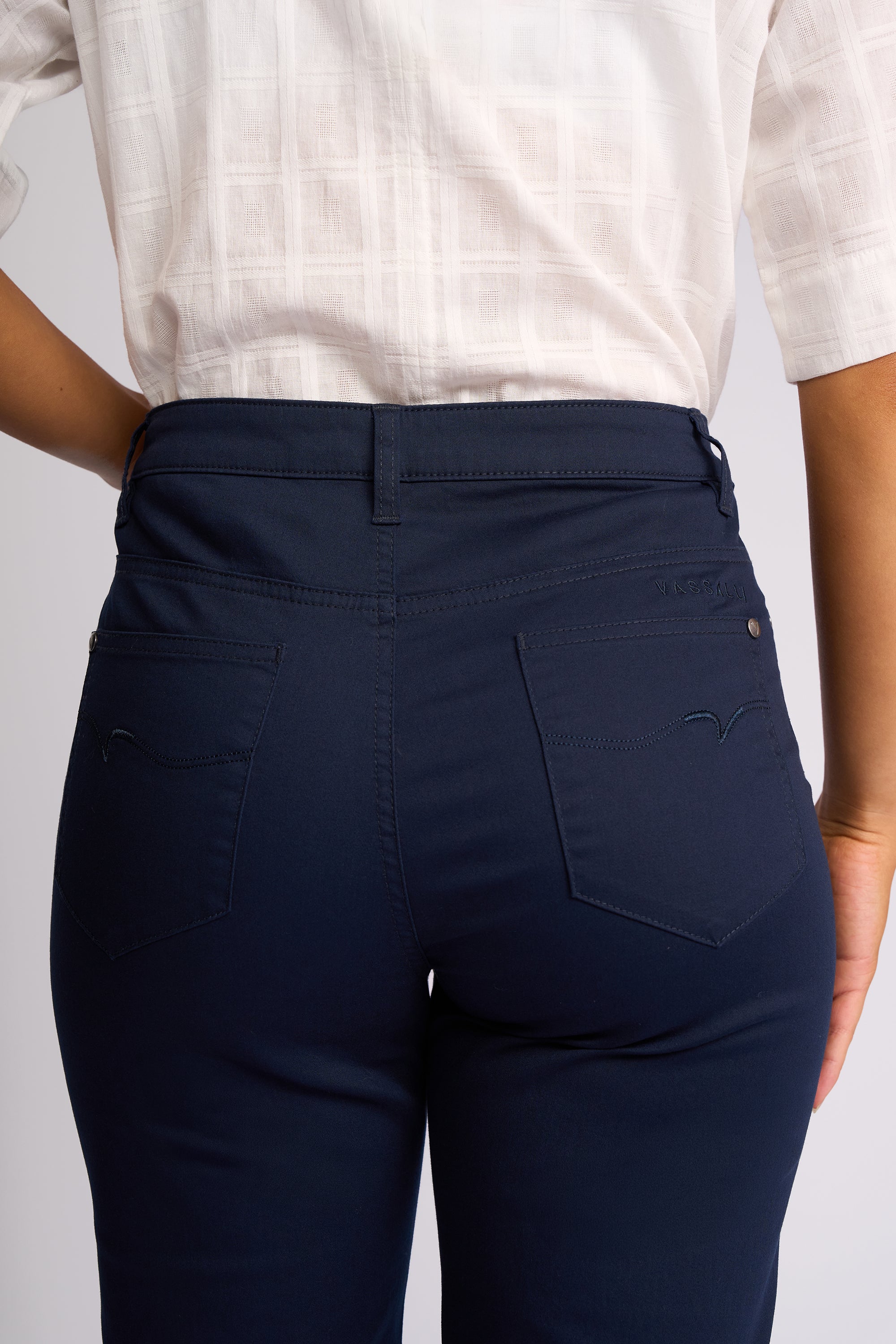 Close-up back view of a person wearing dark navy blue pants with a white patterned short-sleeve top, showing the back pockets and waistband details.