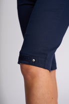 Close-up of a person's leg wearing dark navy blue cropped pants or shorts, showing the rolled cuff with a button tab detail against a light gray background.