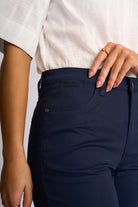 Close-up of a person wearing dark navy blue pants and a white short-sleeve top, with the hand resting on the waistband.